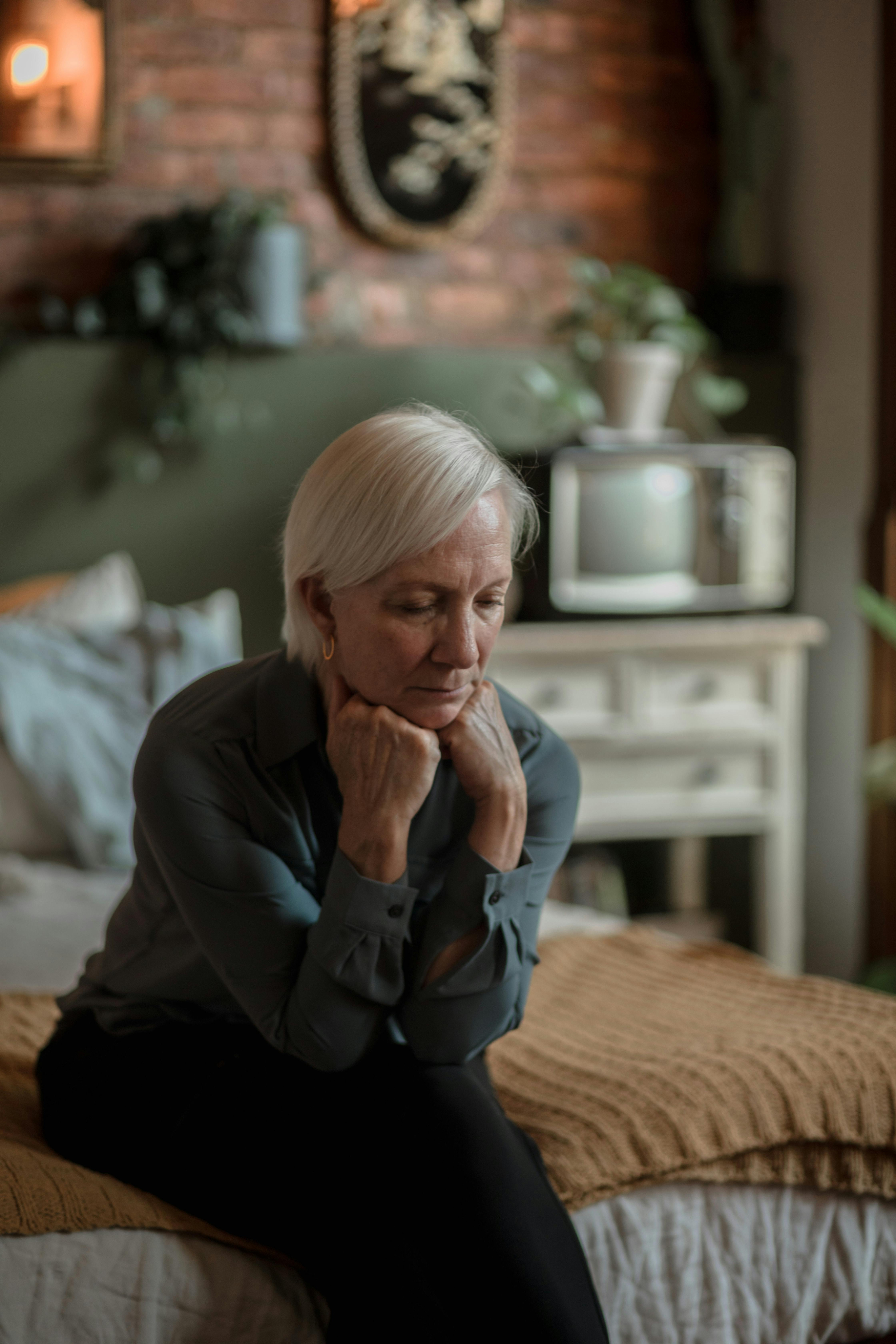 A woman sitting thoughtfully on the edge of a bed.